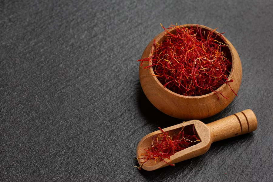a wooden bowl with red Saffron in it next to a wooden spoon